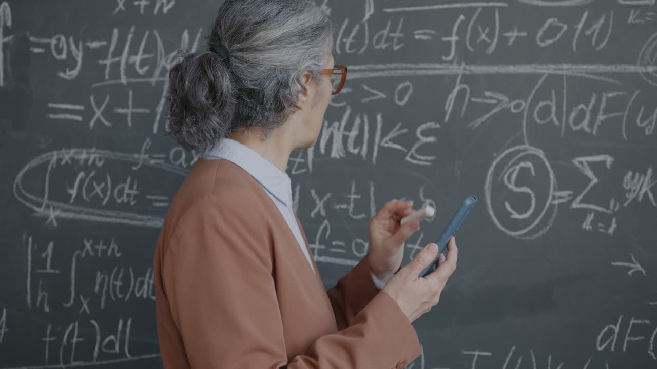 Teacher using a calculator and smartphone in a classroom filled with math equations