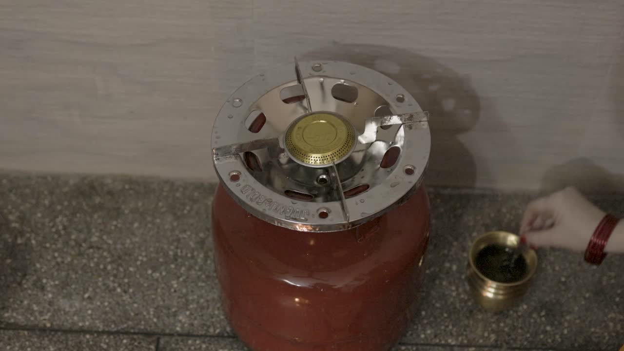 Donne indiane che pregano il dio del fuoco sacro con offerte a casa, con una bombola di gas GPL.
