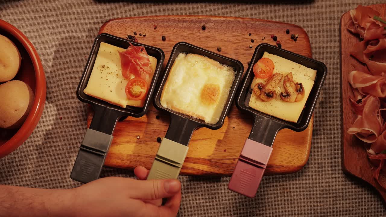 Traditional Swiss melted raclette cheese, hot melted French dish, family cooking dinner with Spanish style tapas ingredients and grill.