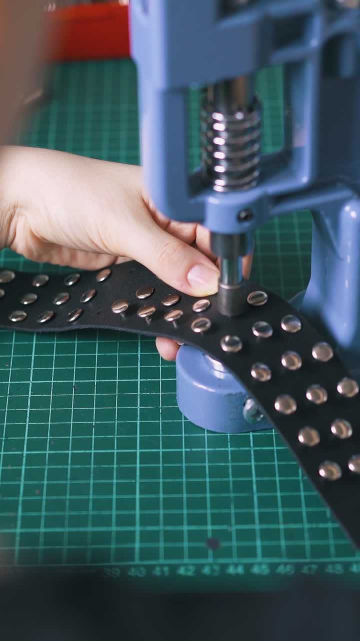 CU: Woman sets metal accessories on fashionable black leather choker with workshop press machine backside close view