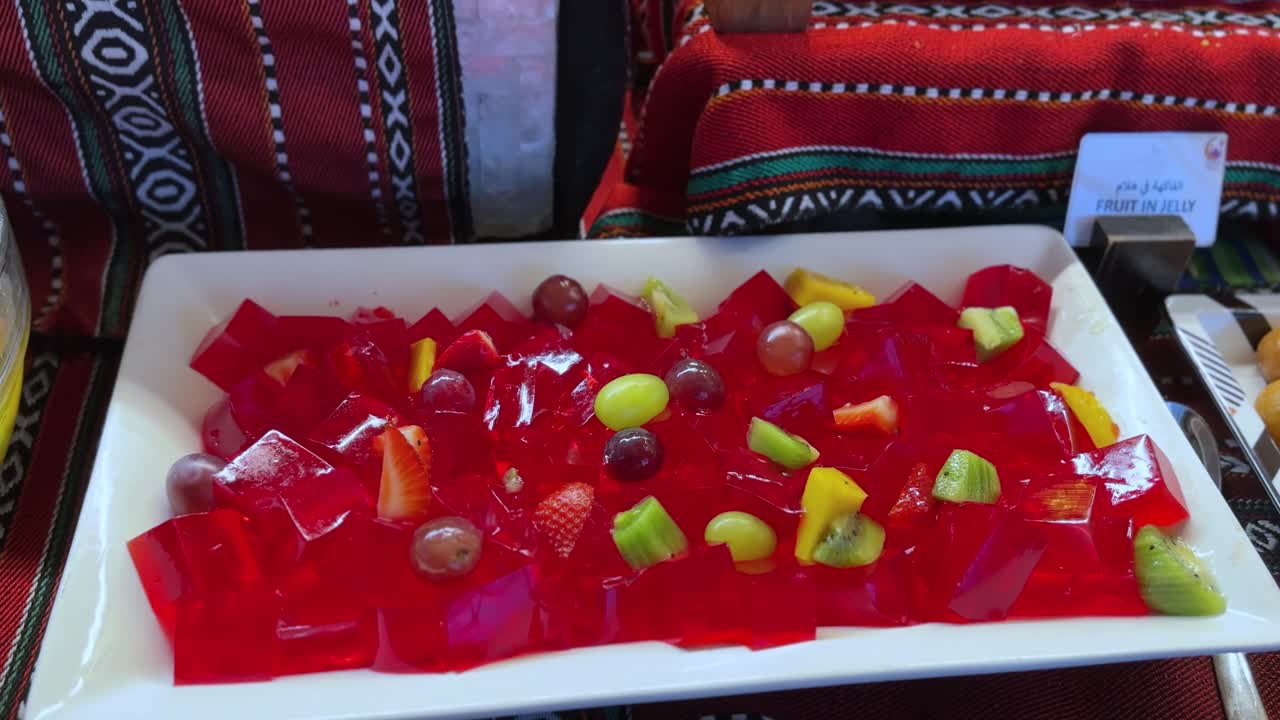 Vibrant 4K close-up of red jelly topped with assorted fruits on a traditional Middle Eastern tablecloth. Ideal for culinary, festive, or cultural food projects.