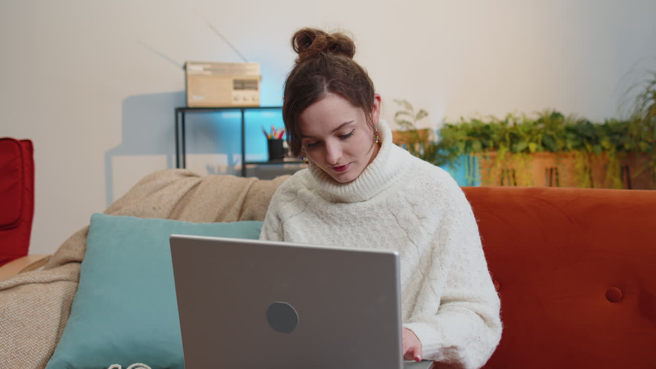 mujer joven independiente sentada en el sofá cerrando la computadora portátil después de terminar el trabajo en la habitación en casa