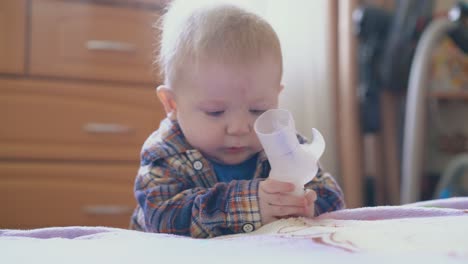 Lustiger-Junge-Knabbert-An-Einem-Teil-Des-Inhalators,-Der-Sich-Auf-Ein-Großes-Weiches-Bett-Stützt