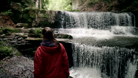 slow motion of a young female tourist enjoying an epic waterfall view.