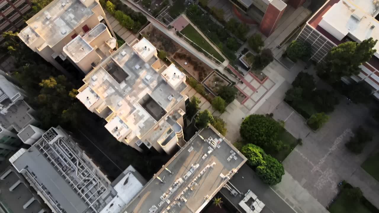 Vista aérea panorâmica do campus da UCLA, diretamente acima dos telhados dos edifícios da universidade, com vista para jardins e calçadas.