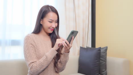 asian thai woman holding mobile phone, posting social media, online shopping, texting, typing text message with one finger sitting by the window