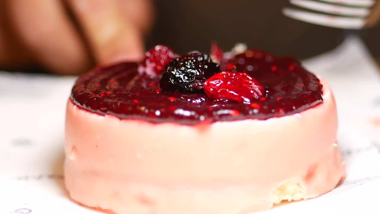 persona comiendo un pequeño pastel de bayas rosas con un tenedor