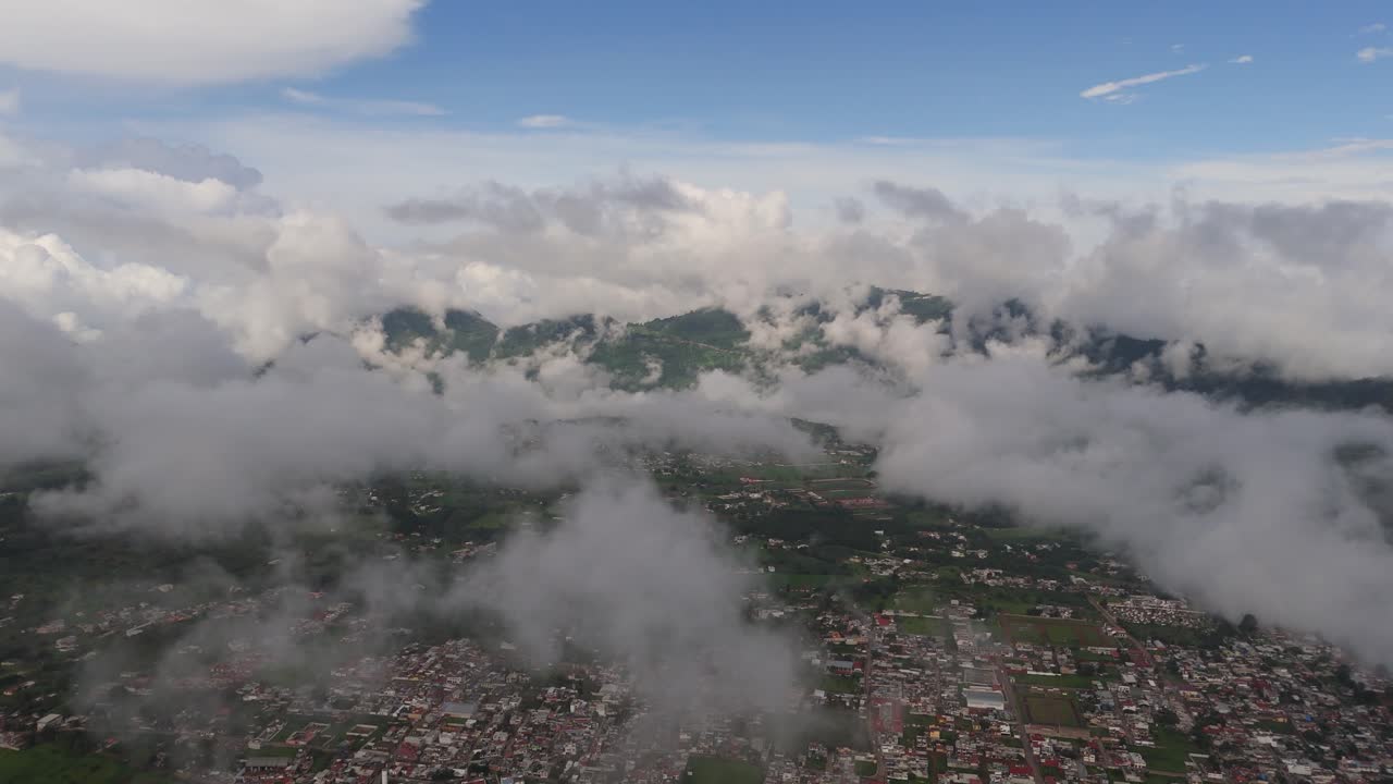 Fluffy clouds hover over small mountain villages nestled in a peaceful valley.
