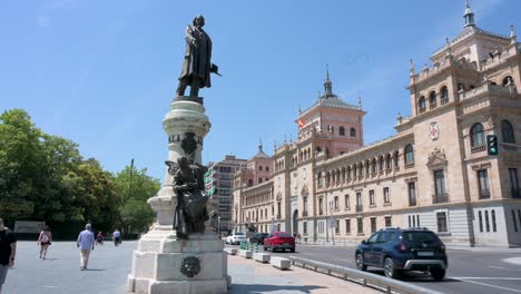 tourists and locals walk past the josé zorrilla statue in the foreground at campo grande park, with the historic academia de caballería (cavalry academy) in the background, valladolid, spain.