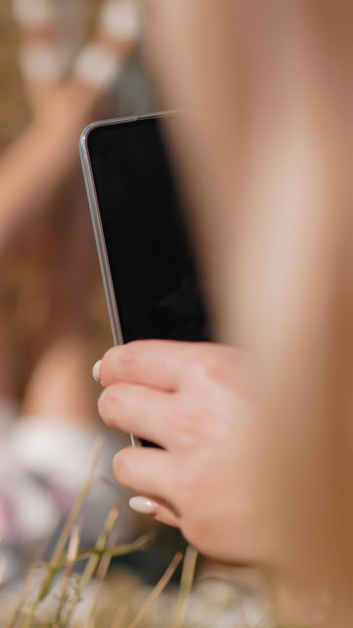 vista de mano de cerca de una persona que sostiene un teléfono inteligente tomando una foto del sujeto tendido en una bala de heno, con un fondo borroso del paisaje rural