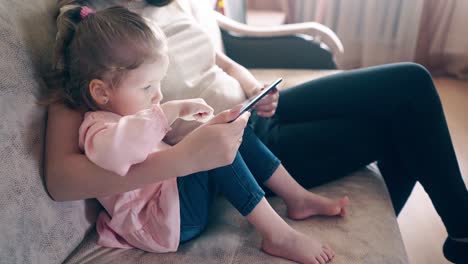 Side-view-4k-oung-attractive-mother-and-sweet-daughter-are-sitting-on-the-couch