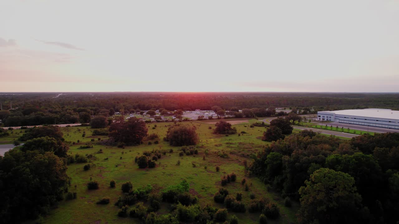 Drone aerial view of Ocala, Florida landscape with fields, trees, and warehouses at sunset, symbolizing growth and development