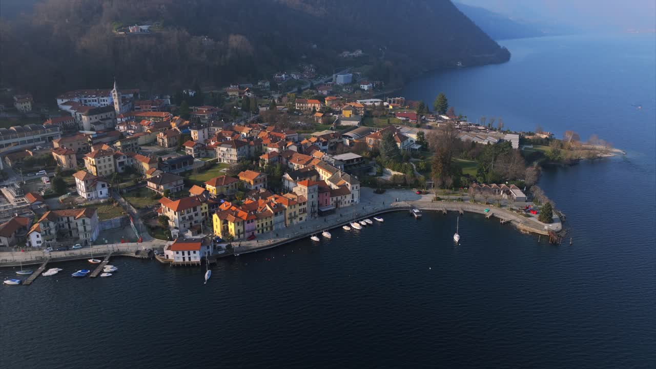 Pella village on Lake Orta, Italy, with buildings and boats along waterfront at dusk. Aerial drone