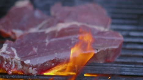 bistecs de carne de res cocidos por las llamas en la parrilla de barbacoa en cámara lenta con humo que se levanta de las brasas calientes debajo de 4k