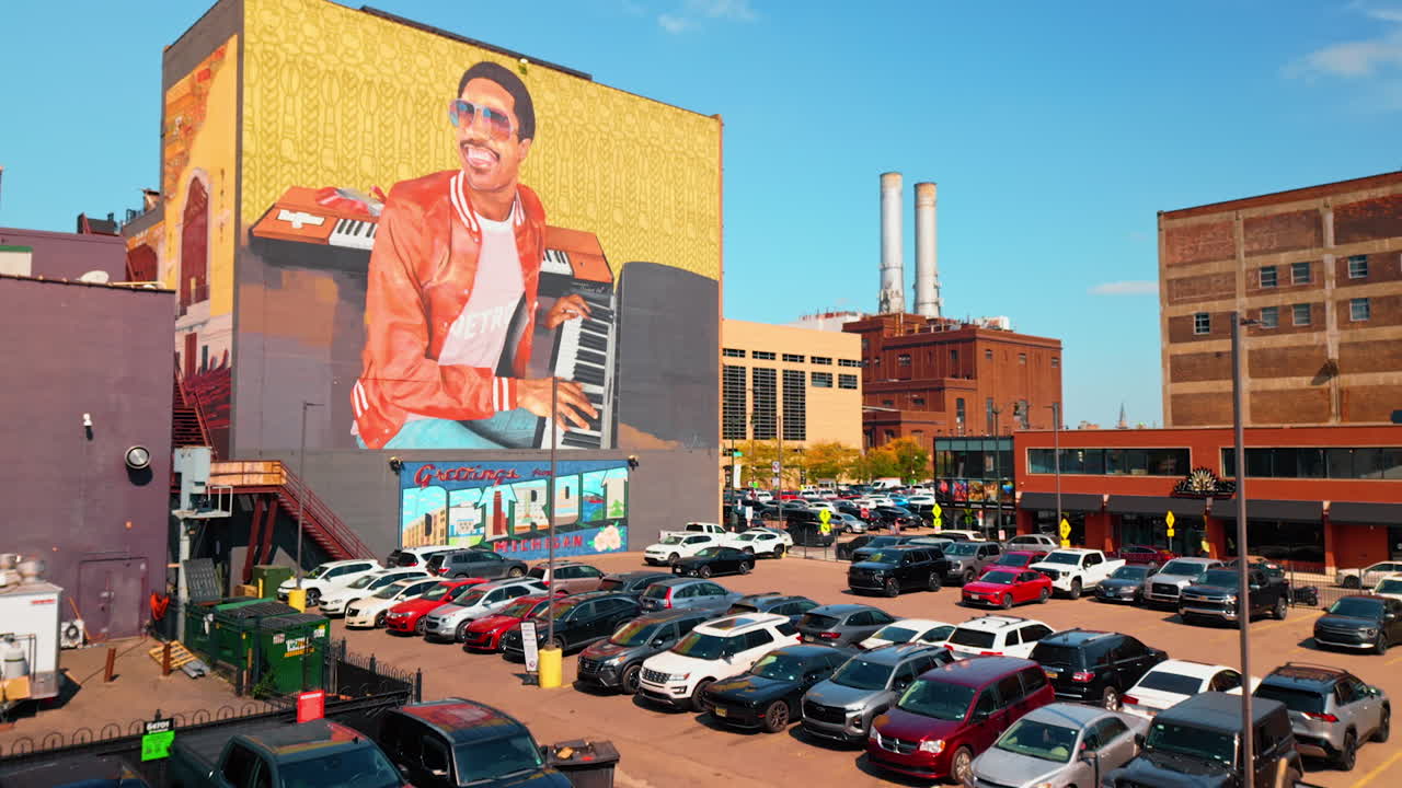 Detroit, USA, 28 July 2025: Footage over the parking lot busy with cars. Approaching the building with mural of an African-American musician. Detroit, Michigan, USA