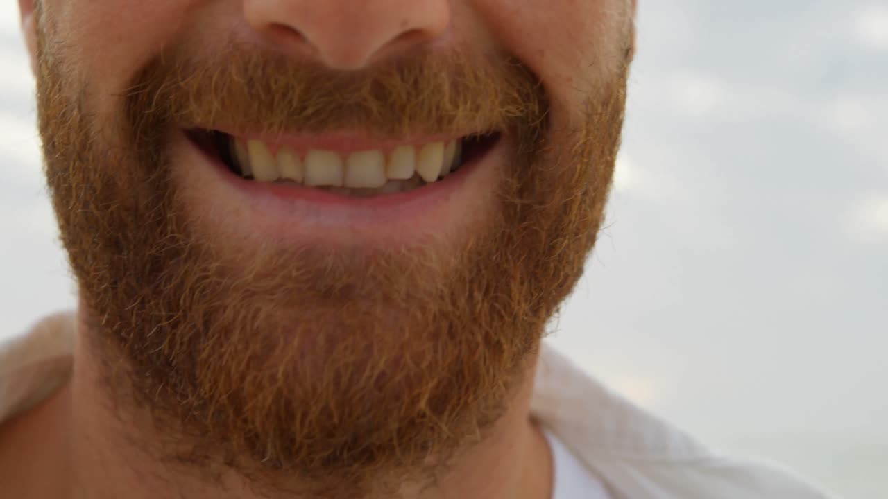 Close-up young happy caucasian man in beard smiling on the beach 4k
