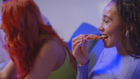 grupo de amigos de la generación z sentados en el sofá en casa comiendo pizza para llevar y hablando 1