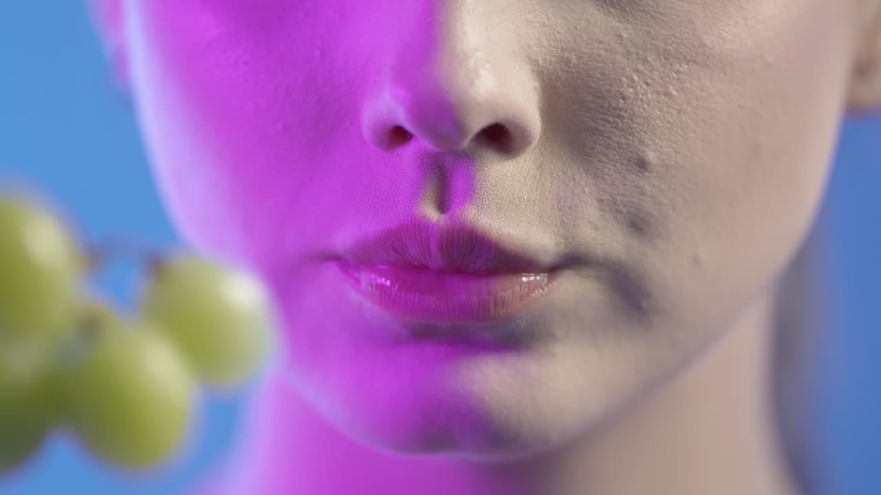 Close-up of a woman's face with magenta lighting and a grape