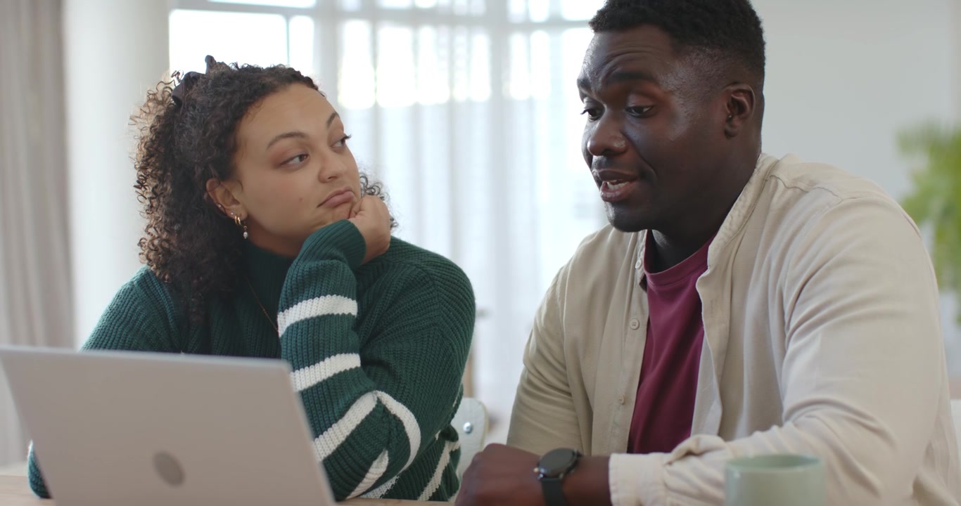 Couple at home table, man starting typing and pointing on laptop, explaining content, woman smiling