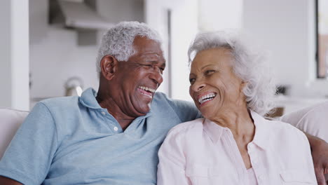 Retrato-De-Una-Amorosa-Pareja-De-Ancianos-Sentados-En-Un-Sofá-En-Casa-Riéndose-Juntos