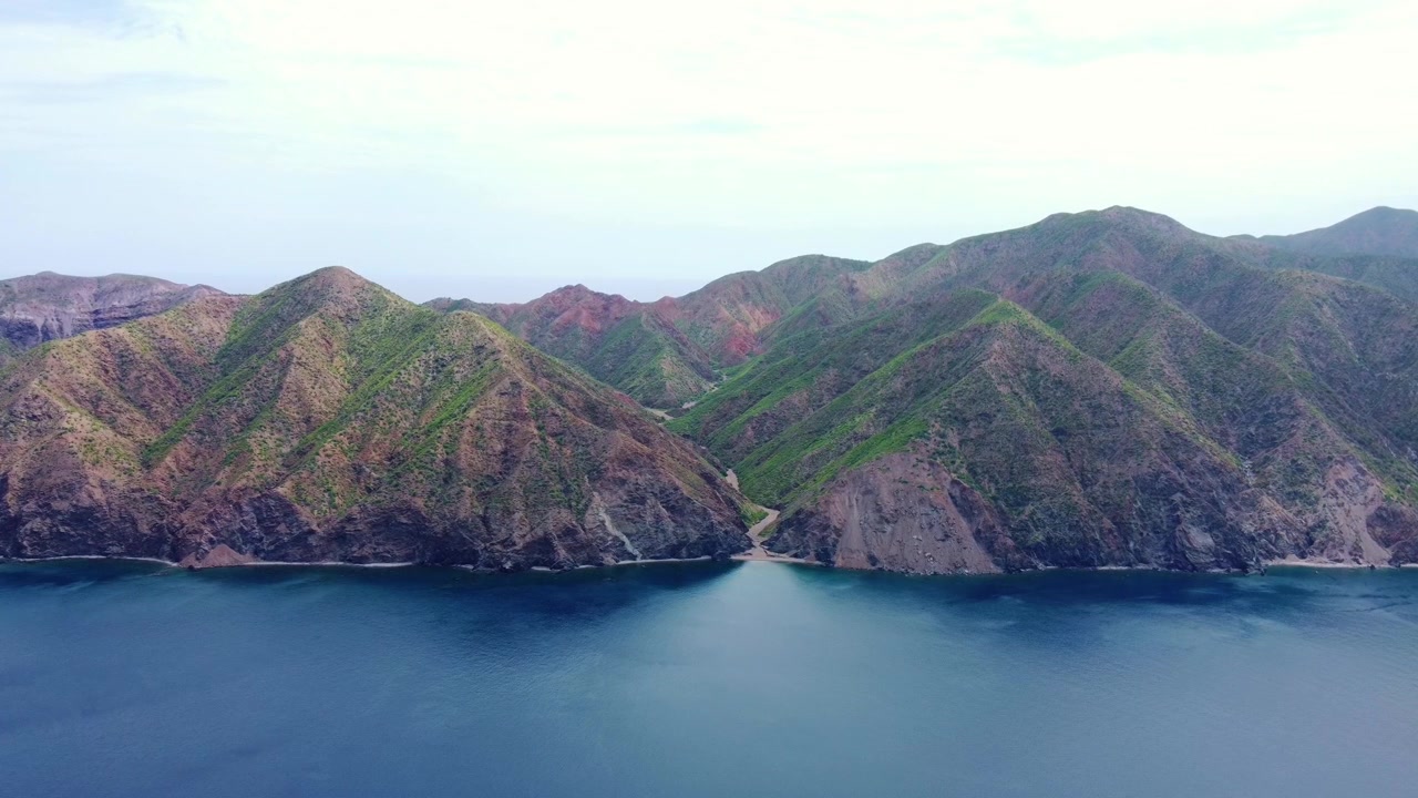 Prospettiva aerea con drone ad alta quota che mostra le imponenti creste montuose dell'Isola di Cerralvo che si estendono lungo il mare calmo e blu a La Ventana, Messico
