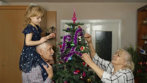 Kleines-Süßes-Mädchen-Mit-Der-Familie-Der-älteren-Großeltern,-Die-Zu-Hause-Einen-Künstlichen-Weihnachtsbaum-Schmücken