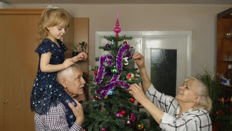 niña linda con abuelos mayores familia decorando árbol de navidad artificial en casa