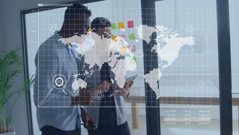 two male colleagues using glass wall in tech office, sketching data points on digital map overlay
