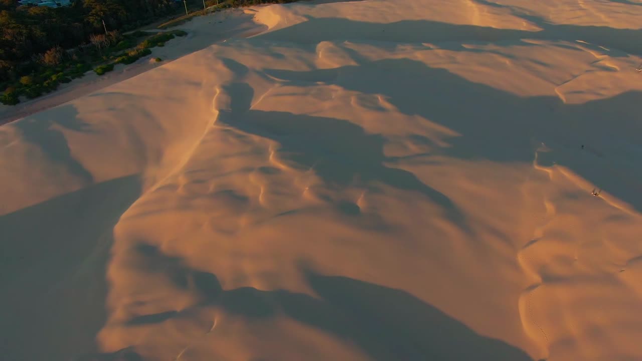 An expansive birds-eye view of long shadows cast by sand dunes during sunset.
