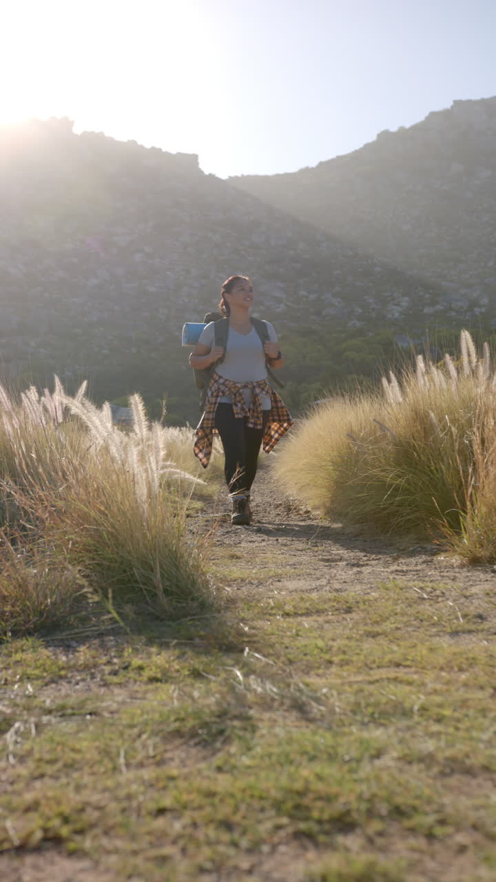 Vertical video: Hiking on mountain trail, woman carrying backpack and yoga mat, enjoying nature