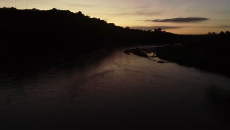 predawn aerial flight down calm river, golden sky reflecting in water
