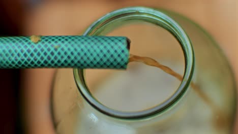 Close-Up-of-Apple-Juice-Flowing-Through-a-Hose-into-a-Glass-Bottle