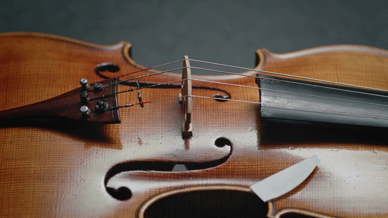Sliding camera revealing varnished violin body in studio to show bridge strings white wedge