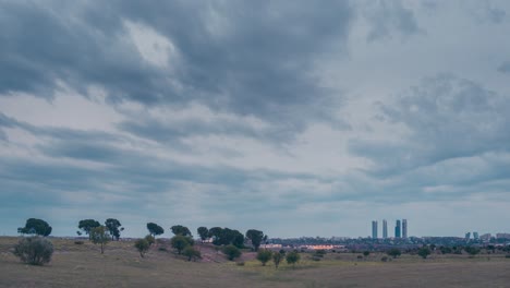 Zeitraffer-Bewölkter-Und-Stürmischer-Himmel-In-Der-Skyline-Von-Madrid-Bei-Sonnenuntergang,-Bäume-Und-Ländliches-Land-Im-Vordergrund