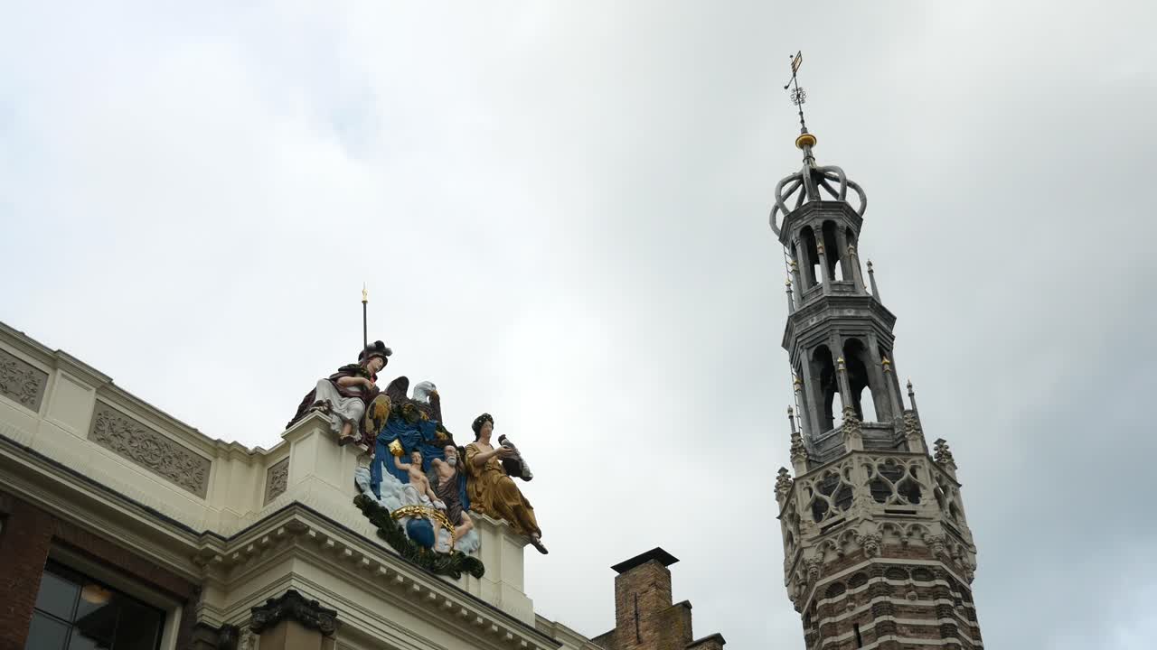 알크마르의 흐린 하늘을 배경으로 교회 탑 옆 건물에 있는 거룩한 조각상을 보여주는 정적 샷