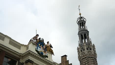 Toma-Estática-Que-Muestra-Estatuas-Sagradas-En-El-Edificio-Junto-A-La-Torre-De-La-Iglesia-Contra-El-Cielo-Nublado-En-Alkmaar