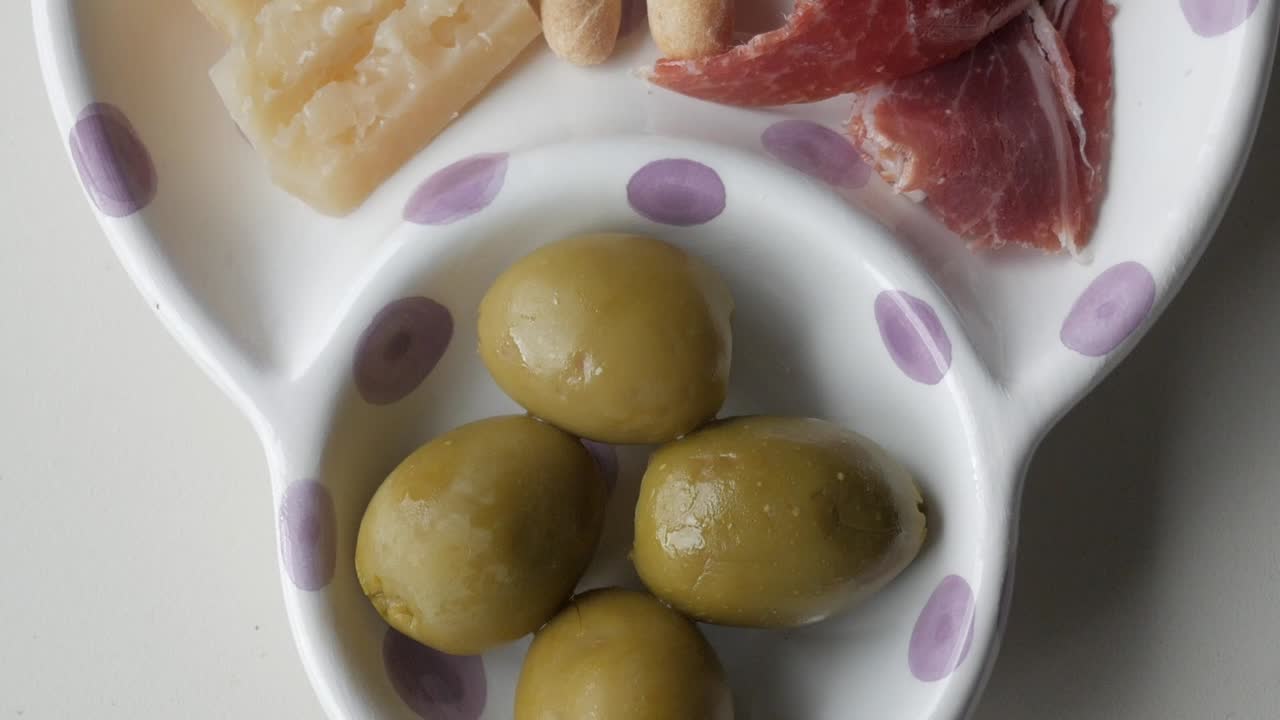 Olives served as part of a Spanish tapas plate with jamon, cheese, and colines