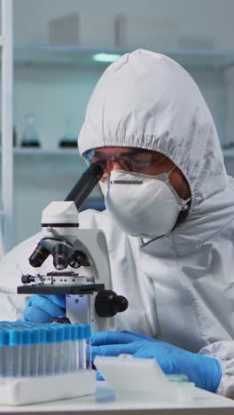 vertical video: close up of scientist looking through a microscope wearing ppe suit