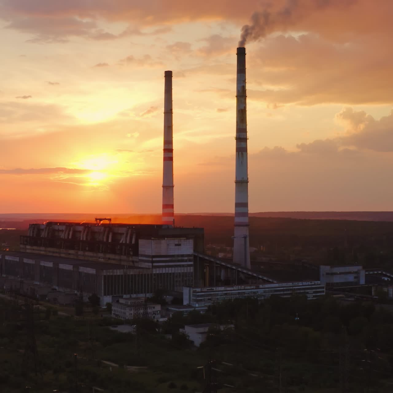 Factory in the evening. Dirty emissions from industrial pipes filling the air at sunset. Ecological problems. Aerial view. Camera rising up.