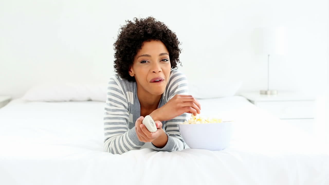 una mujer linda acostada en la cama viendo la televisión.