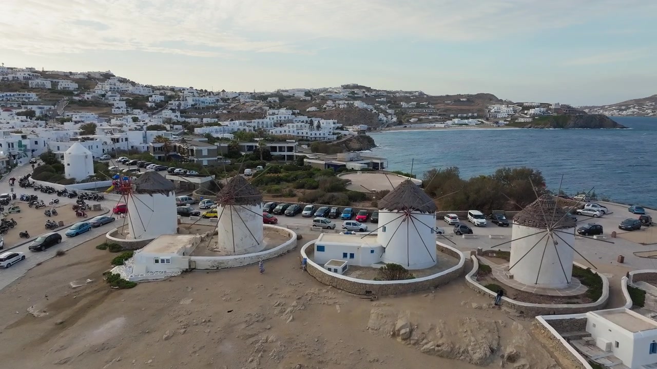 Mulinini della città di Mykonos con fitti edifici bianchi e costa di mare blu, ripresa aerea in dolly