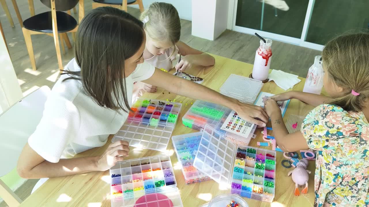 madre e hijas haciendo actividad de perlas en un café