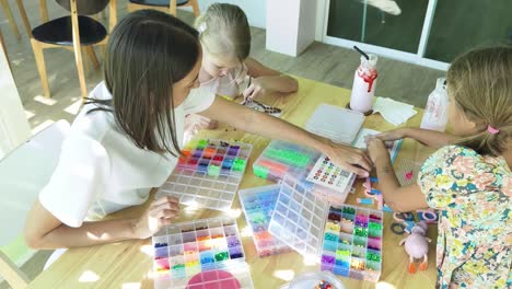 madre e hijas haciendo actividad de perlas en un café