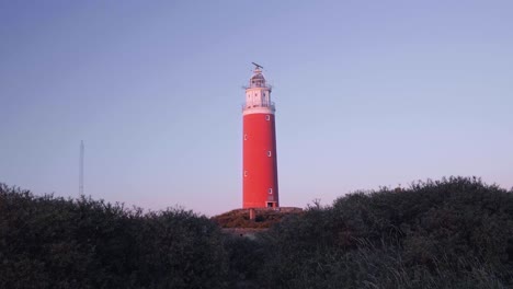 person walking towards red lighthouse on hill at sunset time, texel island, netherlands