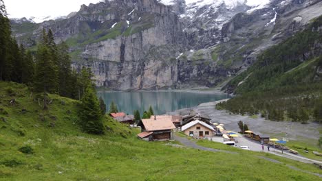 disparo aéreo hacia atrás: vista de 2 excursionistas en su camino a la cafetería de montaña y las montañas gigantes bluemlisalp que rodean el glaciar turquesa szure lago oeschinensee en kandersteg, suiza