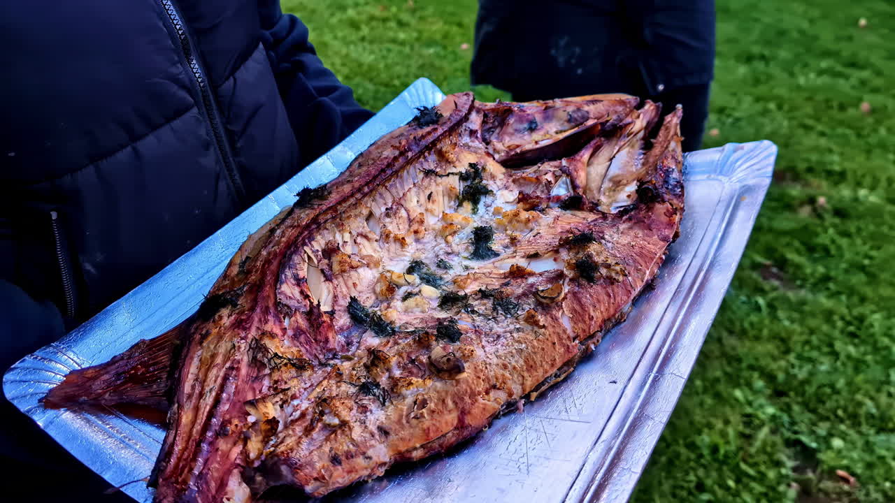 Grilled filleted fish served on metal tray after cooking over charcoal in backyard outdoor setting