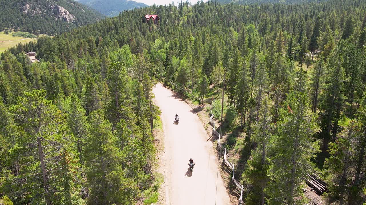 Two motorcycle riders drive towards the camera with an aerial view dolly backwards in the mountains