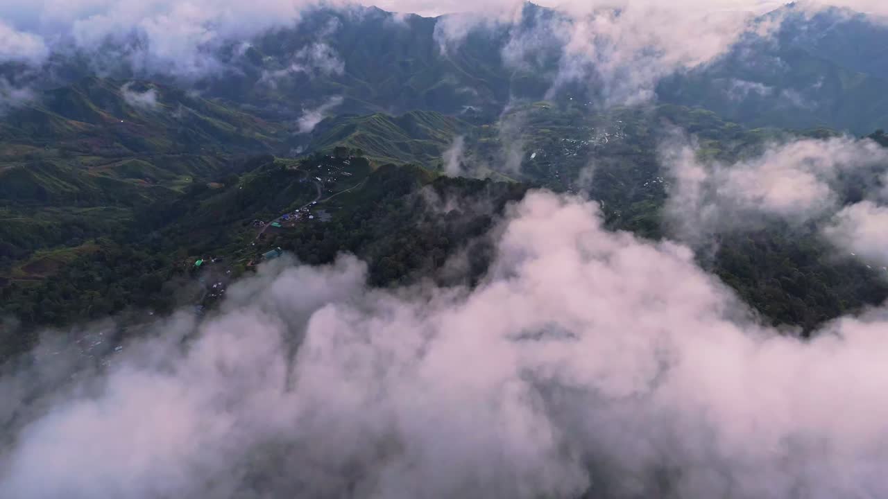 Aerial drone shot of a remote mountain village perched on a green ridge in Davao Philippines. Dramatic thick clouds and mist surround the highland peaks in this scenic landscape