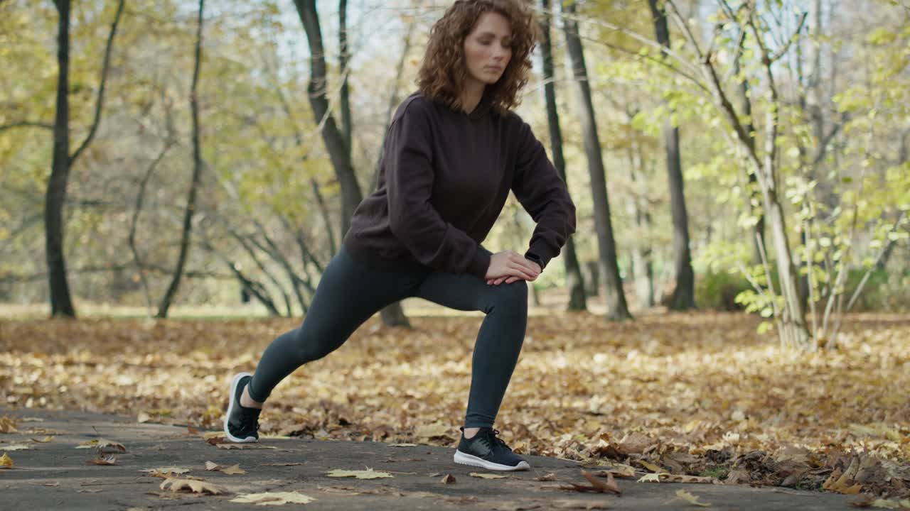 mujer de jengibre calentándose antes de correr en el parque en otoño