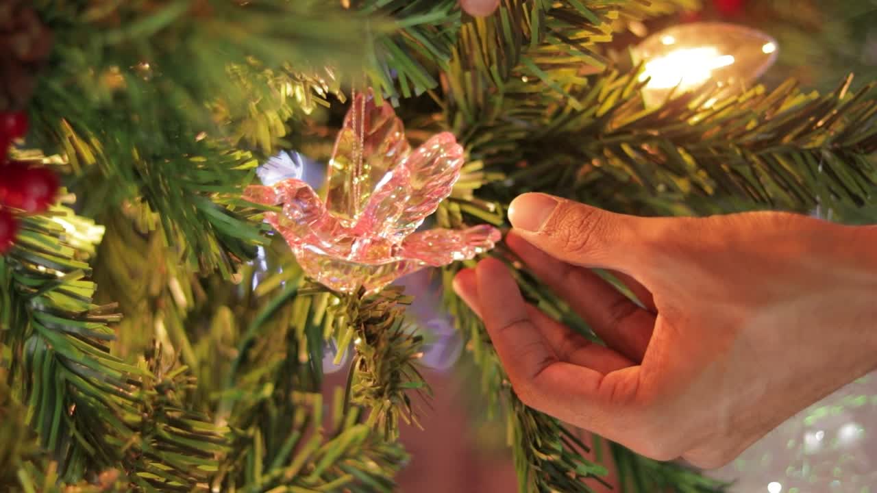 poniendo un ornamento de colibrí de cristal rosa en el árbol de navidad decorado